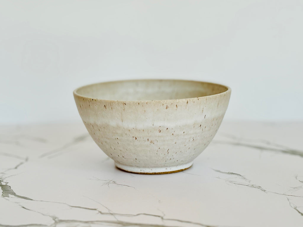 A large beige speckled ceramic bowl on a marbled surface.