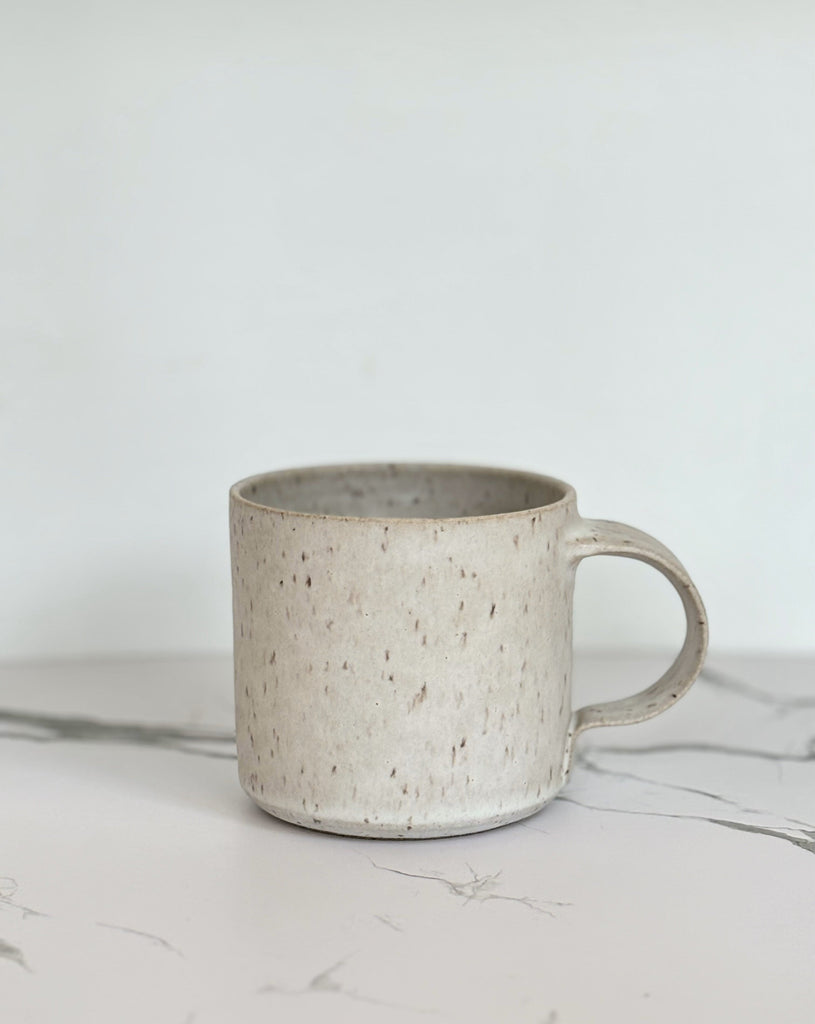 A beige speckled ceramic mug on a marbled surface.