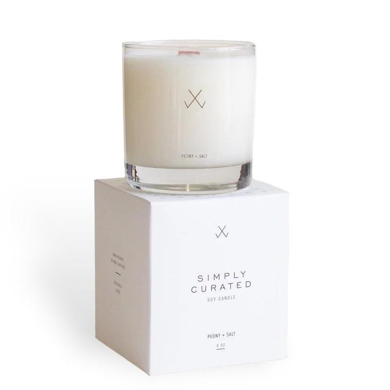 A Simply Curated peony + salt soy candle on its white packaging box with minimalistic branding logo.